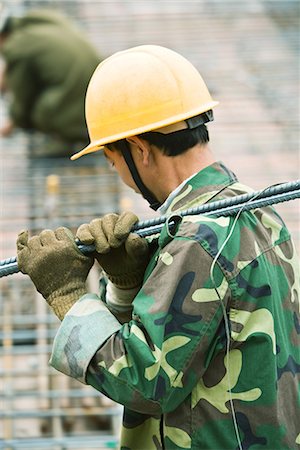 Construction worker wearing camouflage and hard hat carrying metal rod on shoulder, side view Stock Photo - Premium Royalty-Free, Code: 695-03378140