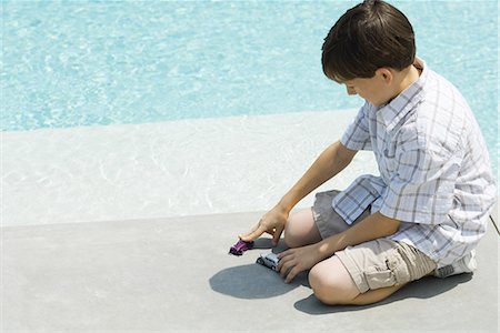 Boy sitting on ground, playing with toy cars, next to pool Stock Photo - Premium Royalty-Free, Code: 695-03378174