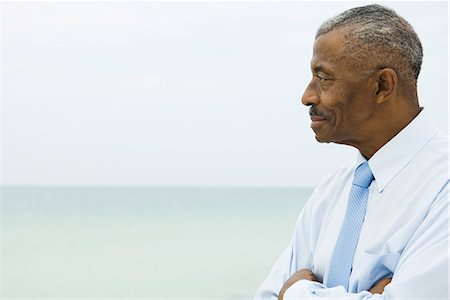 satisfied african american man - Businessman smiling with arms folded, side view, sea in background Stock Photo - Premium Royalty-Free, Code: 695-03378226