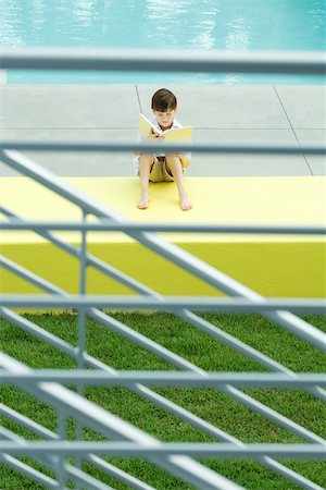 Boy sitting by swimming pool, reading book, viewed through railing Foto de stock - Sin royalties Premium, Código: 695-03378265