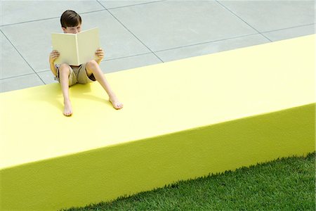 Boy sitting on low wall outdoors, reading book, high angle view Stock Photo - Premium Royalty-Free, Code: 695-03378266