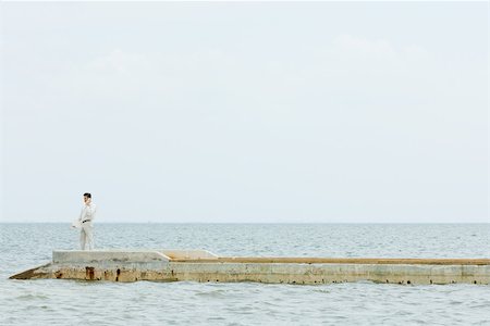 Man standing at the end of pier, using cell phone, in the distance Stock Photo - Premium Royalty-Free, Code: 695-03378279