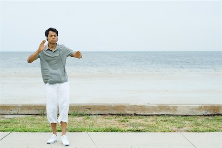 Man standing at the beach with arms out, listening to headphones, eyes closed Stock Photo - Premium Royalty-Free, Code: 695-03378293