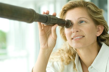 Woman looking through telescope, smiling, close-up Stock Photo - Premium Royalty-Free, Code: 695-03378301