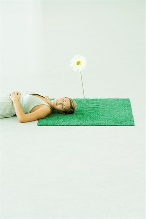 Woman lying on artificial turf next to gerbera daisy, eyes closed Stock Photo - Premium Royalty-Free, Code: 695-03378339