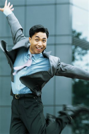 Businessman jumping in the air, arms out, smiling at camera Stock Photo - Premium Royalty-Free, Code: 695-03378360