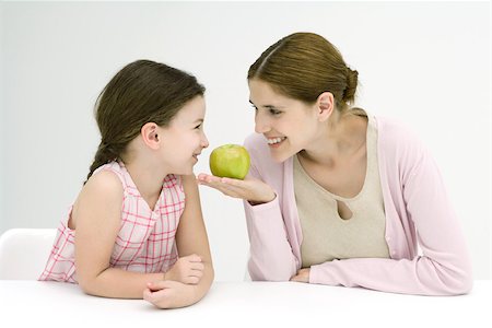 simsearch:695-03378760,k - Mother and daughter sitting face to face, smiling at each other, woman holding apple Foto de stock - Sin royalties Premium, Código: 695-03378462
