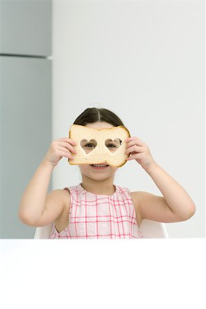 Little girl holding up bread with heart shaped cut outs, looking through holes at camera Stock Photo - Premium Royalty-Free, Code: 695-03378463