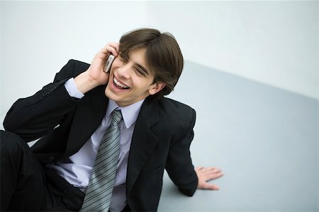 simsearch:695-03378072,k - Young man in suit sitting on the ground, using cell phone, smiling Stock Photo - Premium Royalty-Free, Code: 695-03378500