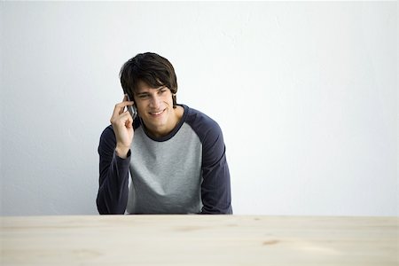 simsearch:695-03380514,k - Young man sitting at table, using cell phone, smiling Stock Photo - Premium Royalty-Free, Code: 695-03378502
