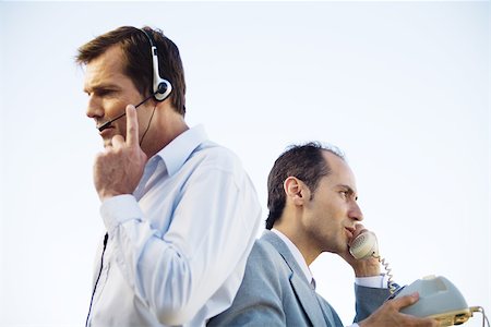 small business phone outside - Two businessmen back to back, one using headset, the other using landline phone, side view Stock Photo - Premium Royalty-Free, Code: 695-03378516
