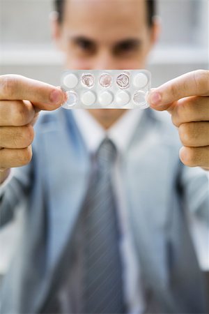 Businessman holding up package of tablets, looking at camera, focus on foreground Stock Photo - Premium Royalty-Free, Code: 695-03378513