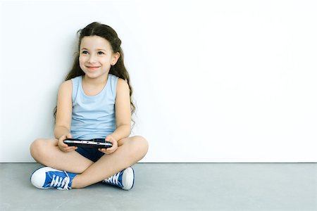 Little girl sitting on the ground, playing handheld video game, smiling Stock Photo - Premium Royalty-Free, Code: 695-03378596