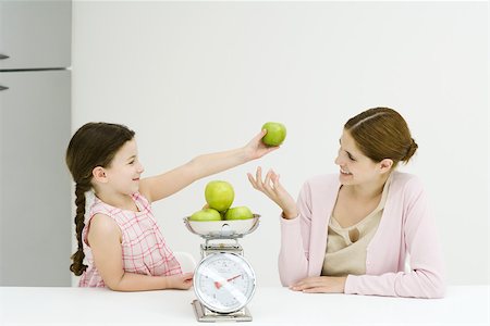 Mère et fille pesant de pommes sur échelle, souriant à l'autre, fille brandissant une pomme Photographie de stock - Premium Libres de Droits, Code: 695-03378613