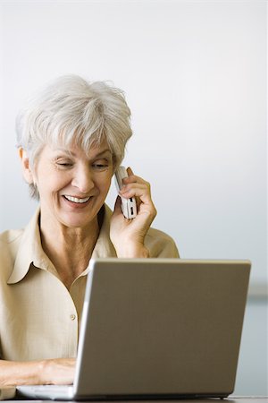 simsearch:632-02344964,k - Senior woman using laptop computer and cell phone, smiling, looking down Stock Photo - Premium Royalty-Free, Code: 695-03378665