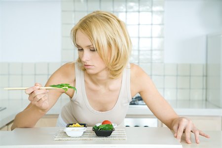 simsearch:695-03390179,k - Young woman leaning over kitchen counter, picking up herbs with chopsticks Foto de stock - Sin royalties Premium, Código: 695-03378752