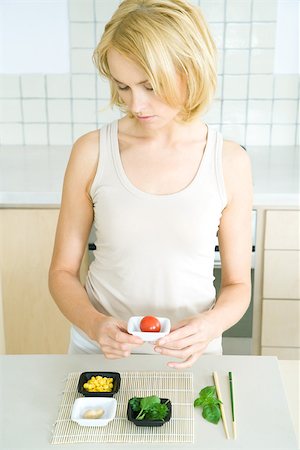 simsearch:695-03378760,k - Young woman standing in kitchen, holding cherry tomato in small dish, looking down Foto de stock - Sin royalties Premium, Código: 695-03378753