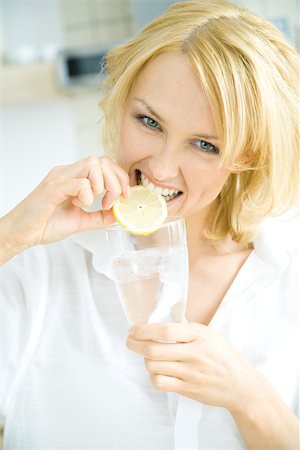 Woman holding glass of water, biting into lemon slice, looking at camera Stock Photo - Premium Royalty-Free, Code: 695-03378768