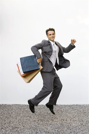 Businessman holding shopping bags, jumping in midair, full length Stock Photo - Premium Royalty-Free, Code: 695-03378897