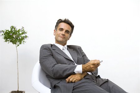 simsearch:633-02044233,k - Businessman sitting, listening to MP3 player, smiling at camera Stock Photo - Premium Royalty-Free, Code: 695-03378900