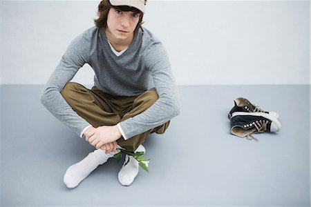 Young man sitting on the ground next to his shoes, holding flower, looking at camera Stock Photo - Premium Royalty-Free, Code: 695-03378929