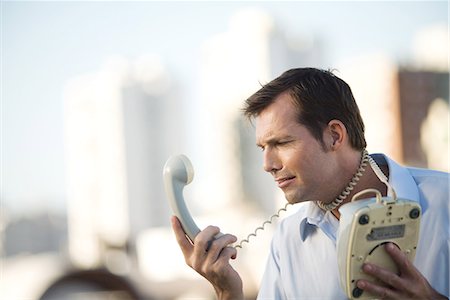 falta de comunicação - Man wrapping landline phone cord around neck, looking at receiver Foto de stock - Royalty Free Premium, Número: 695-03378942