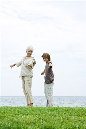 simsearch:696-03401990,k - Grandmother and grandson standing outdoors with arms out, both smiling at camera, ocean in background Stock Photo - Premium Royalty-Free, Code: 695-03379009