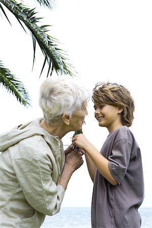 simsearch:696-03401990,k - Grandmother and grandson standing face to face, holding palm leaf, smiling at each other Stock Photo - Premium Royalty-Free, Code: 695-03379010