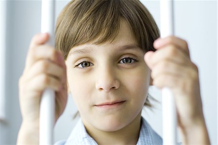 simsearch:695-03379065,k - Boy behind bars, smiling at camera, portrait Foto de stock - Royalty Free Premium, Número: 695-03379077