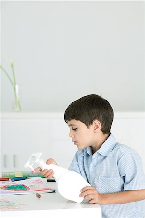 Little boy cleaning crayon scribbles off of table, holding spray bottle Stock Photo - Premium Royalty-Free, Code: 695-03379178