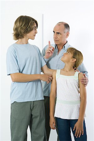 rivalidade entre irmãos - Father shaking his finger at teen son, preteen daughter watching and smiling Foto de stock - Royalty Free Premium, Número: 695-03379172