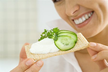 dimpled - Young woman holding up cracker topped with cucumbers and cheese spread, cropped Stock Photo - Premium Royalty-Free, Code: 695-03379296