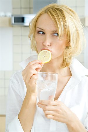 Jeune femme mordre dans une tranche de citron, à la recherche de suite, tenant un verre d'eau Photographie de stock - Premium Libres de Droits, Code: 695-03379304