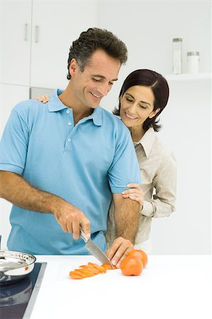 simsearch:695-03378918,k - Couple standing together in kitchen, man slicing tomato, both smiling Fotografie stock - Premium Royalty-Free, Codice: 695-03379479