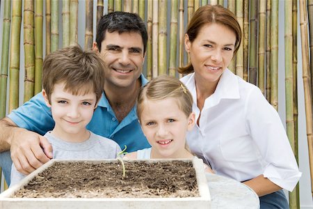 family yard work - Family together, smiling at camera, potted seedling in foreground Stock Photo - Premium Royalty-Free, Code: 695-03379470