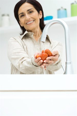 simsearch:695-03378760,k - Woman rinsing roma tomatoes under faucet, smiling at camera Foto de stock - Sin royalties Premium, Código: 695-03379480