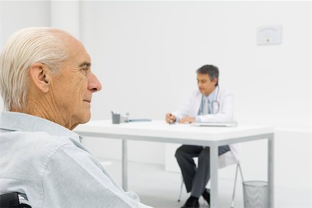 sitting in doctors office waiting - Doctor working at desk, focus on senior patient in foreground Stock Photo - Premium Royalty-Free, Code: 695-03379559