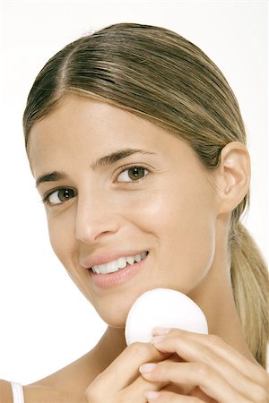 simsearch:633-02128635,k - Woman using powder puff on cheek, smiling at camera Stock Photo - Premium Royalty-Free, Code: 695-03379589