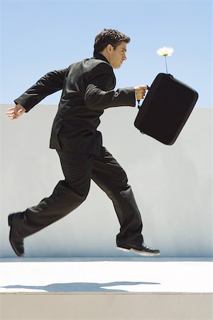 Businessman running in midair, holding briefcase with flower sticking out, side view Stock Photo - Premium Royalty-Free, Code: 695-03379593