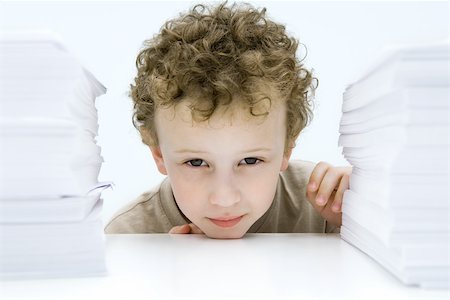 Curly haired boy peering between stacks of paper, smiling at camera Stock Photo - Premium Royalty-Free, Code: 695-03379607