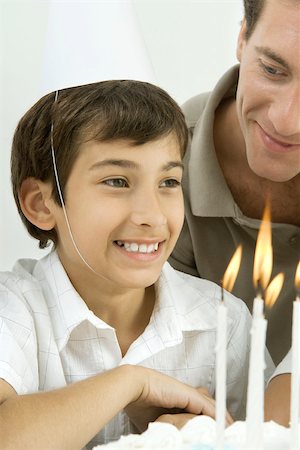 simsearch:695-05763215,k - Boy next to birthday cake with lit candles, wearing party hat, smiling Stock Photo - Premium Royalty-Free, Code: 695-03379675