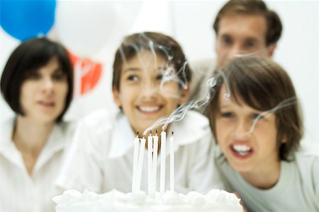 Boys blowing out candles on birthday cake, parents in background Stock Photo - Premium Royalty-Free, Code: 695-03379676