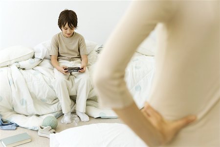 deshecho - Boy sitting in messy room, playing handheld video game, mother in foreground with hand on hip, cropped view Foto de stock - Sin royalties Premium, Código: 695-03379708