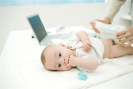 Mother changing baby's diaper on desk, laptop in background Stock Photo - Premium Royalty-Free, Code: 695-03379727