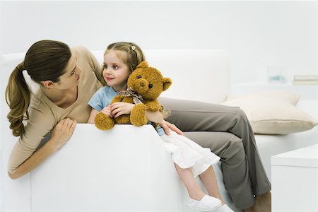 simsearch:633-05401631,k - Mother and daughter sitting on couch, smiling at each other, girl holding teddy bear Stock Photo - Premium Royalty-Free, Code: 695-03379729