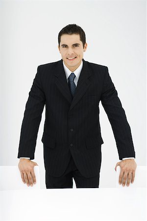 Homme d'affaires souriant à la caméra, debout, les mains sur une chaise, portrait Photographie de stock - Premium Libres de Droits, Code: 695-03379742