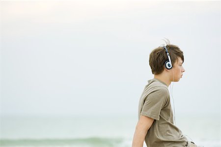 Teen boy sitting on beach listening to headphones, side view Stock Photo - Premium Royalty-Free, Code: 695-03379834