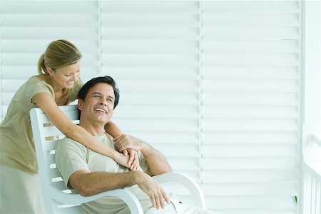 Man sitting in chair, woman standing behind, embracing, smiling Stock Photo - Premium Royalty-Free, Code: 695-03379901