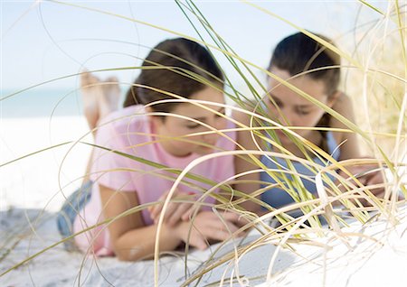 Two teenage girls lying on beach, seen through dune grass Stock Photo - Premium Royalty-Free, Code: 695-03373456
