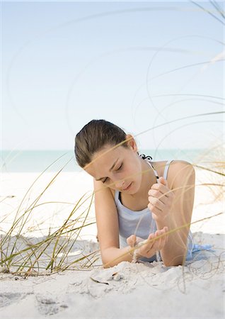 Girl lying on beach, letting sand run through hands Stock Photo - Premium Royalty-Free, Code: 695-03373452